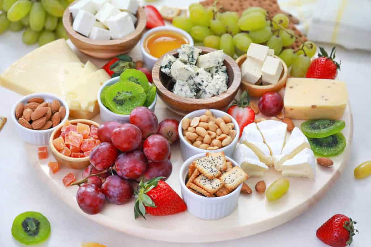 Vegetarian cheese board served on a wooden platter with cheeses, fruits, nuts, condiments, crackers.