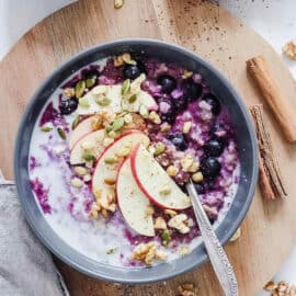 Photo of the perfect bowl of oatmeal with oats, milk, fruit, berries, and nuts in a grey blue bowl in a guide for how to make oatmeal taste good without sugar.