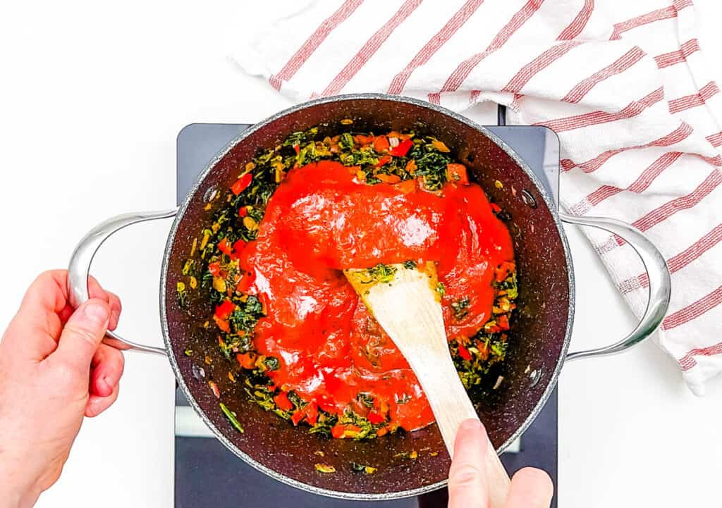 Marinara sauce added to cooked veggies in a large pan.