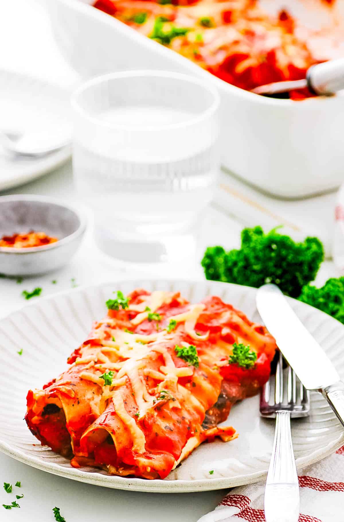 Lasagna roll ups served on a white plate, with a fork and knife on the side.