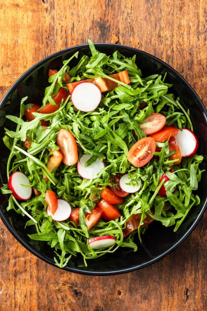 Spinach and arugula salad with tomatoes served in a dark grey salad bowl.