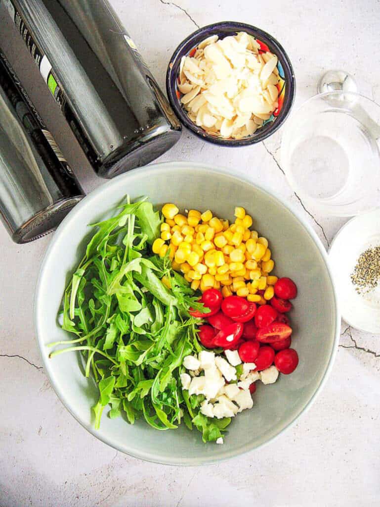 ingredients for spinach and arugula salad with Tomatoes and Goat Cheese: corn, cherry tomatoes, goat cheese, slivered almonds, olive oil, balsamic vinegar, salt, pepper - top view