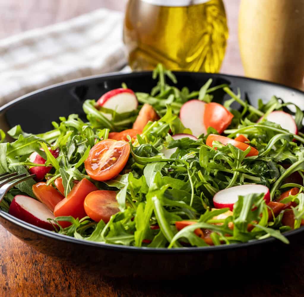 Spinach and arugula salad with tomatoes served in a dark grey salad bowl.