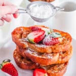Vegan french toast served on a white plate with berries and powdered sugar.