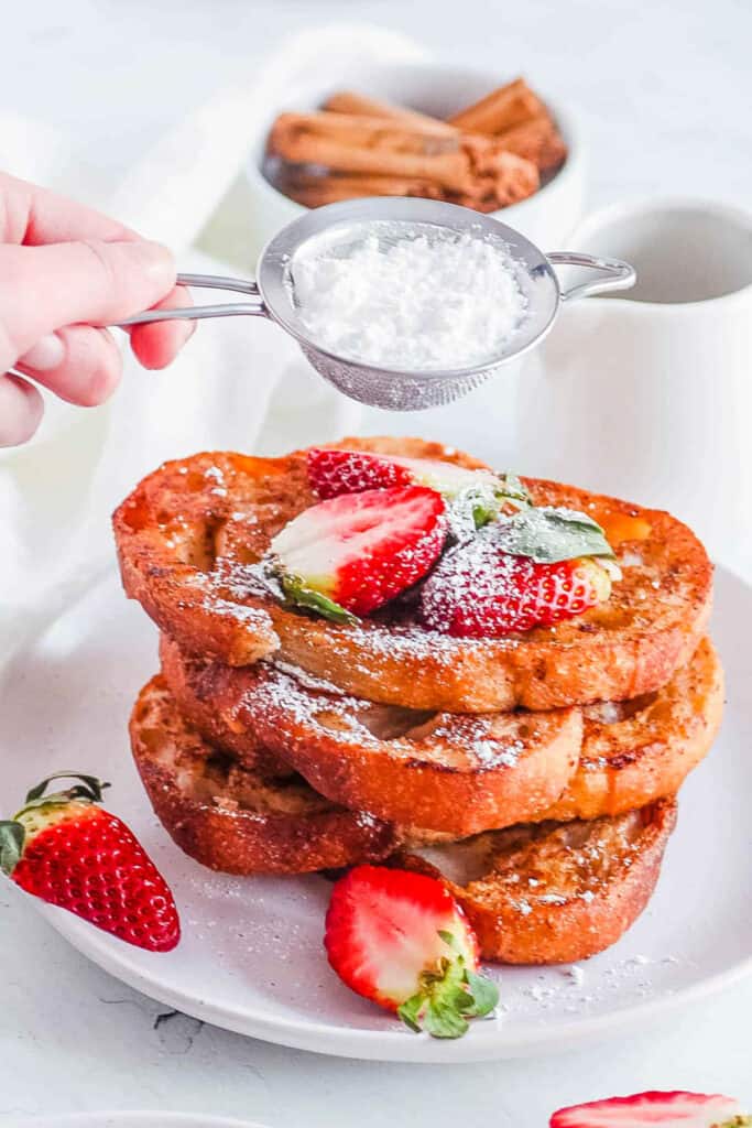 Vegan french toast served on a white plate with berries and powdered sugar.