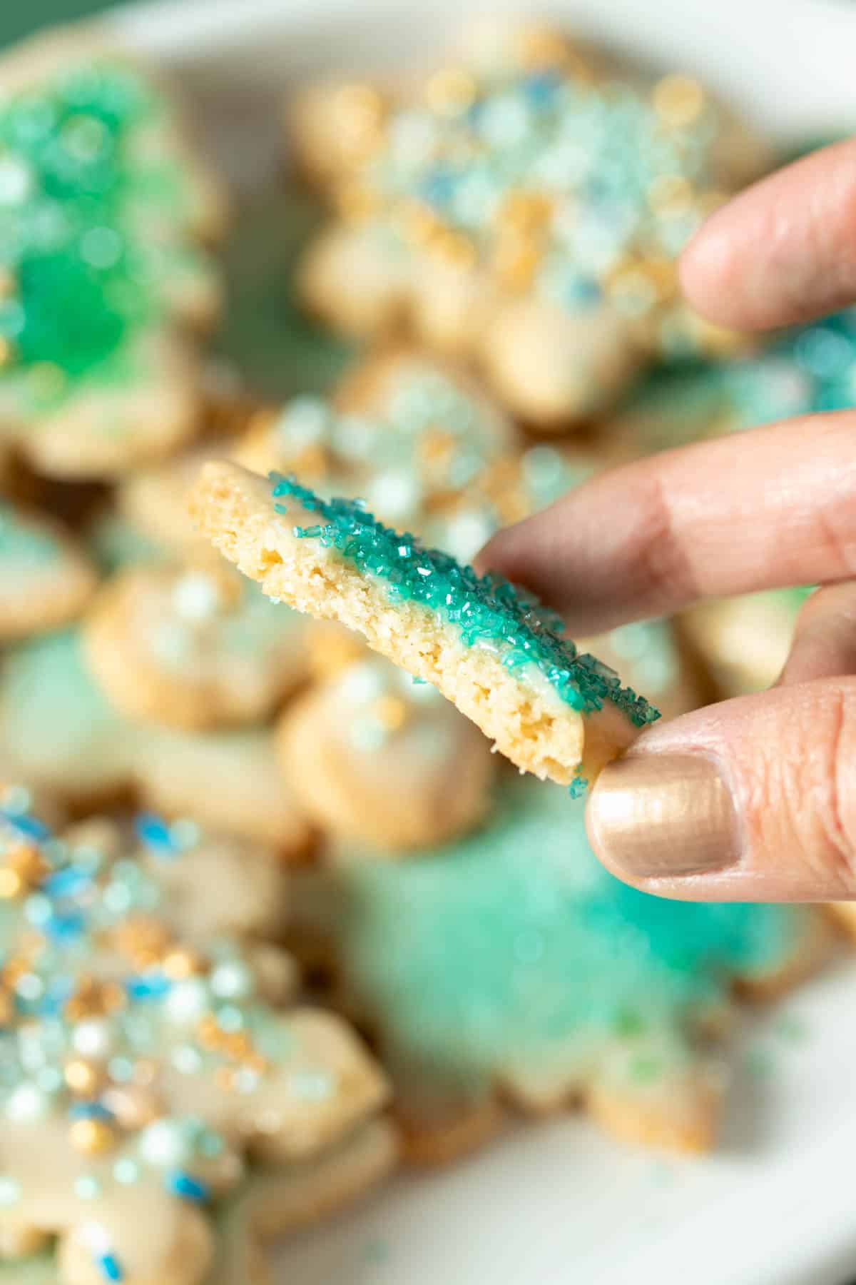 A hand holding a vegan sugar cookie with a bite out of it sideways so you can see the inside.