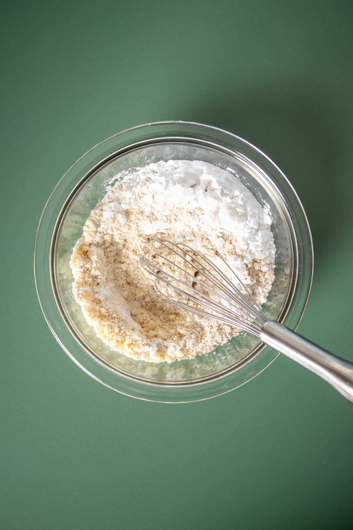 Top view of a glass bowl with a whisk mixing flours inside.