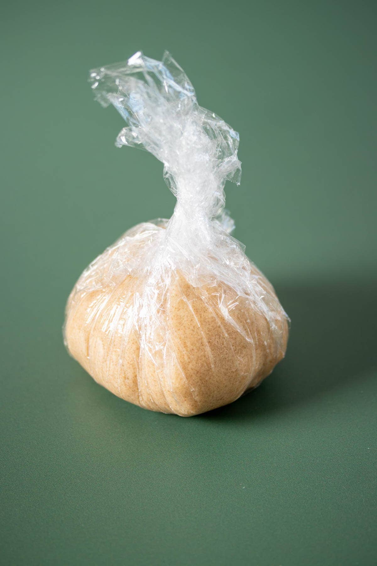 Sugar cookie dough in a ball wrapped in plastic wrap sitting on a green surface.