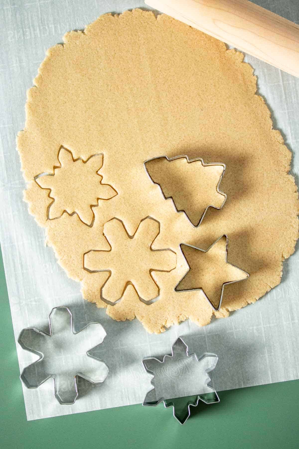 Rolled out cookie dough on a piece of parchment paper with cookies cutters cutting shapes.