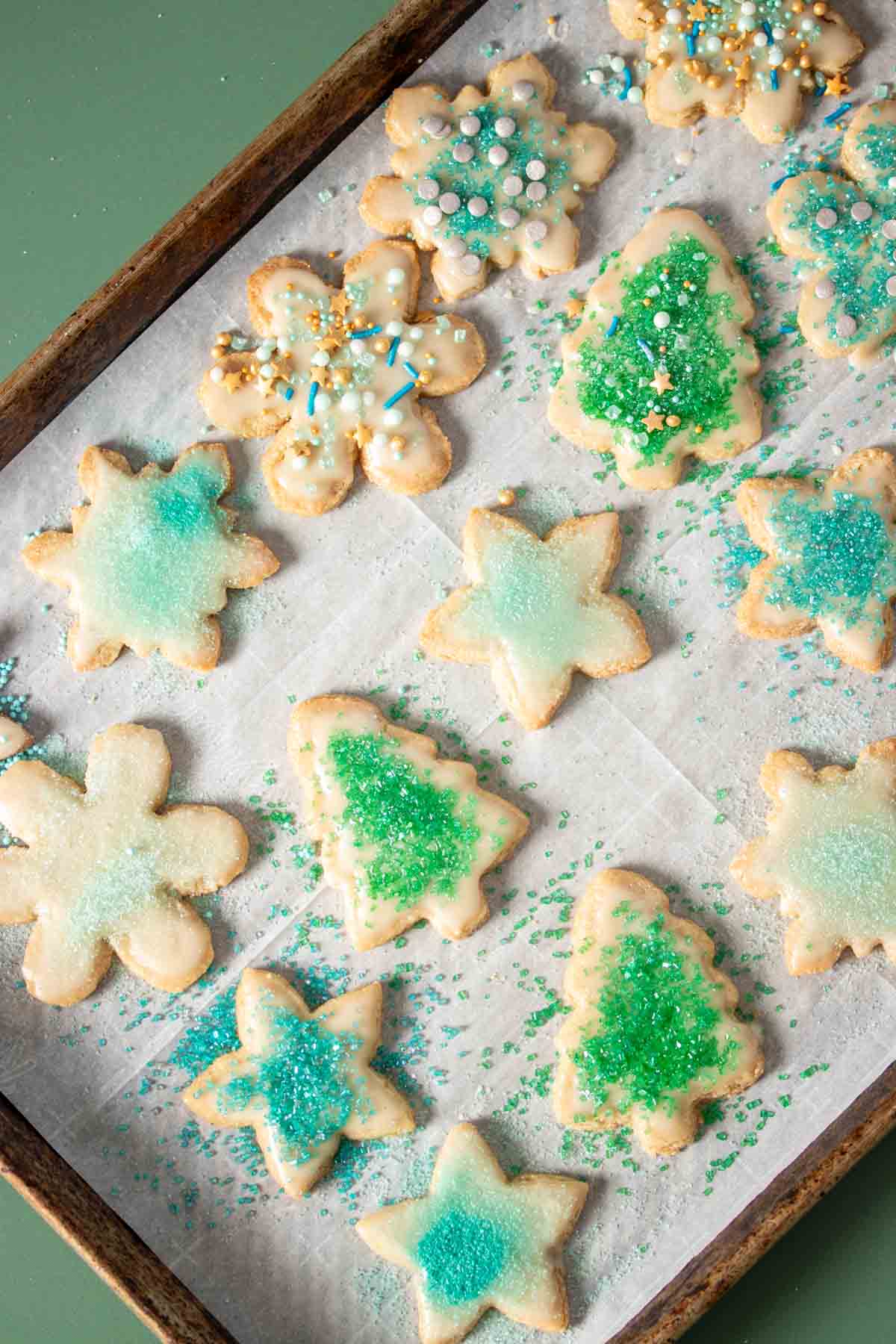 Holiday shaped vegan gluten free sugar cookies decorated with green and blue decor on a parchment lined baking sheet.