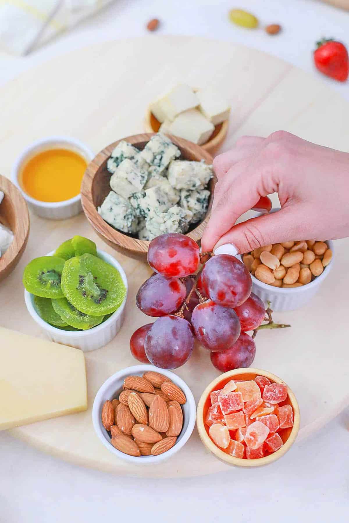 Hand holding grapes above a veggie charcuterie board.