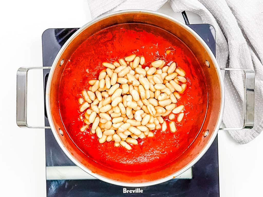 Cannellini beans added to a large pot with tomato sauce and spices.