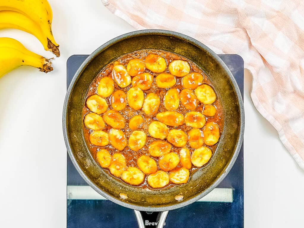 Bananas sauteeing with brown sugar and ،er in a pan.