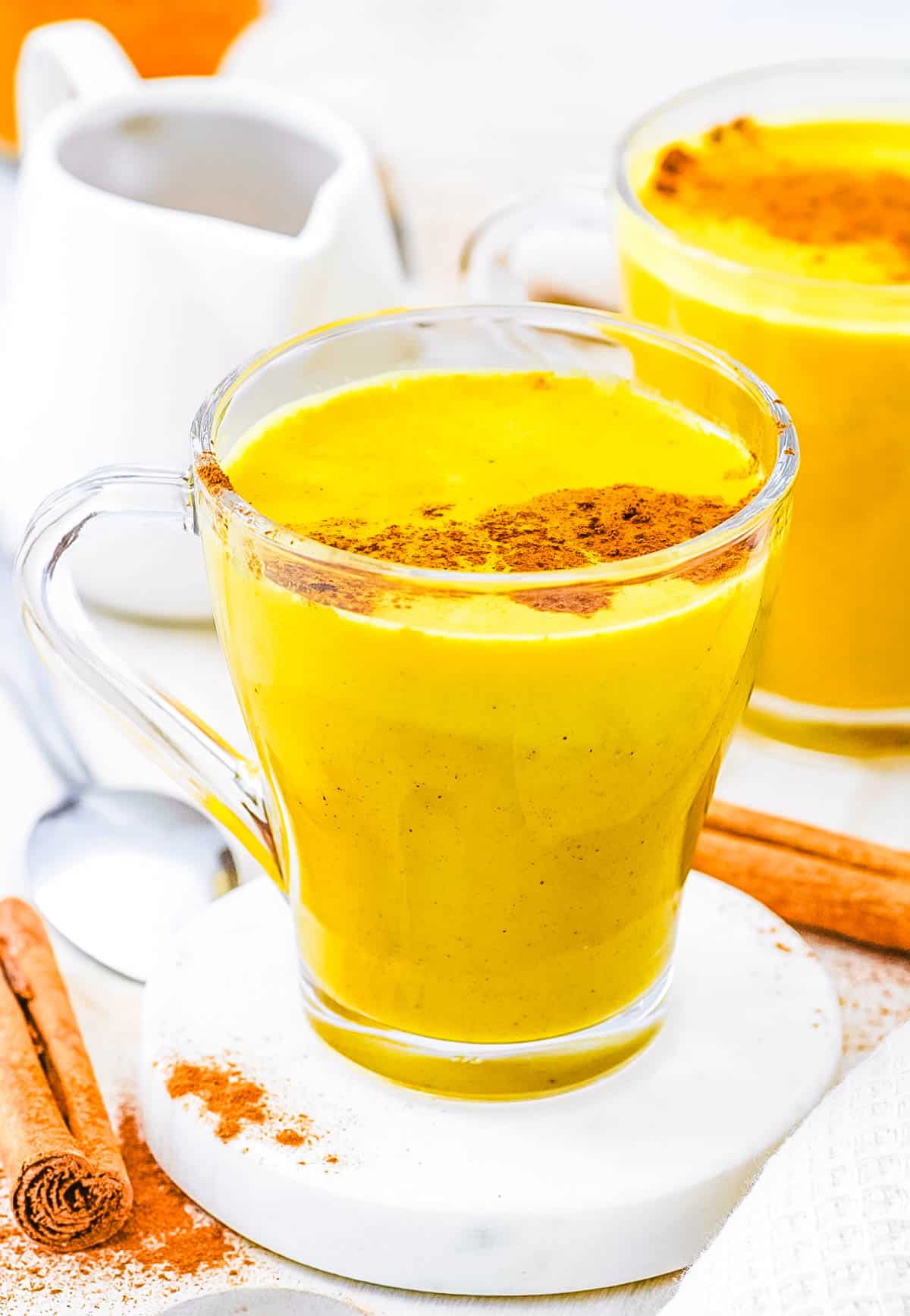 Golden turmeric milk latte, served in a gl،, topped with cinnamon.
