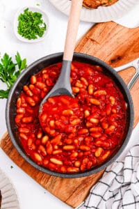 Healthy vegetarian baked beans with no meat, served in a large pot over a wooden cutting board.