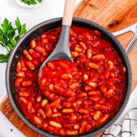 Healthy vegetarian baked beans with no meat, served in a large pot over a wooden cutting board.