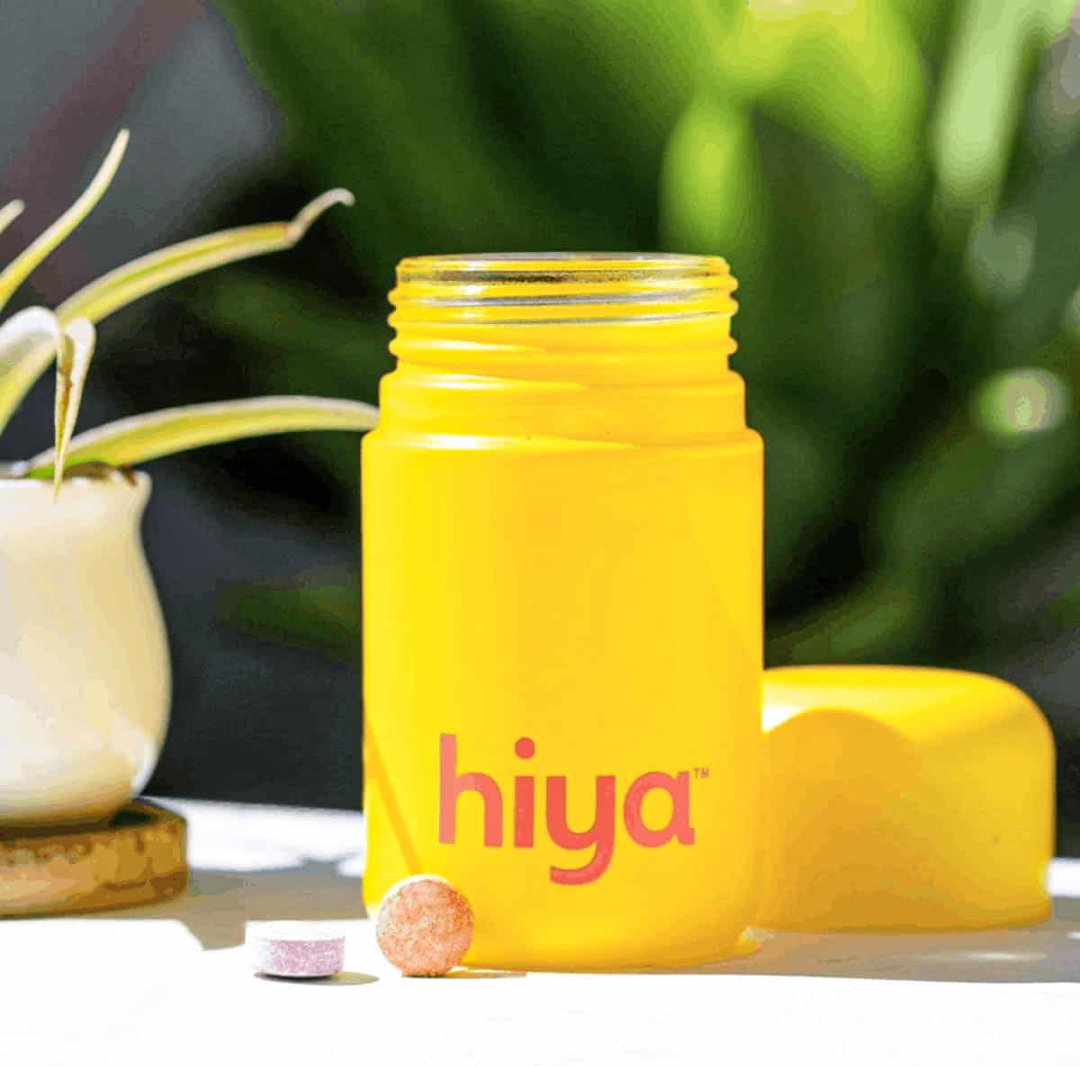 Open Hiya vitamins bottle with two vitamins sitting in front of the bottle.