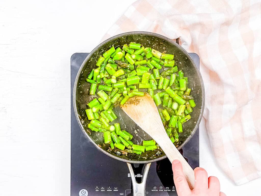 Asparagus pieces being sauteed in a pan.