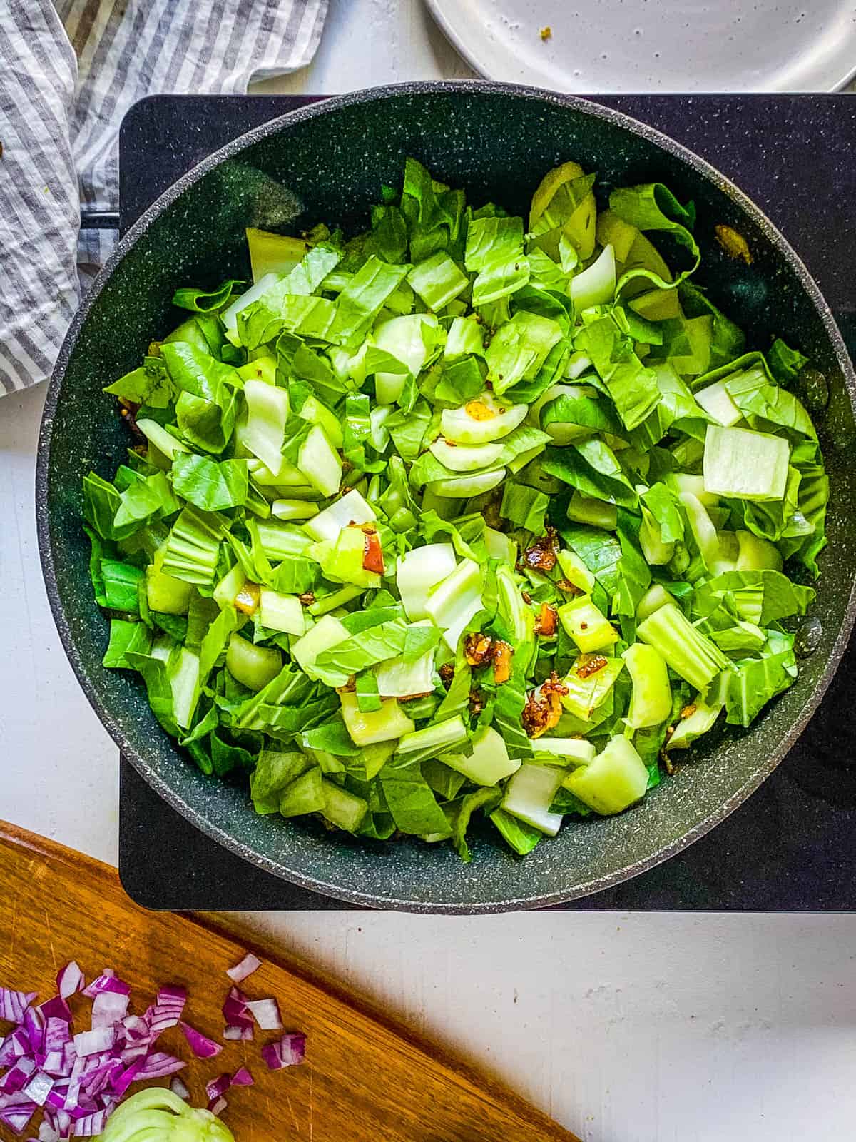 Bok choy cooking with Indian spices in a large skillet on the stove.