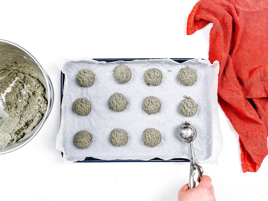 Cookie scoop scooping out balls of cookie dough and placing them on a baking sheet lined with parchment paper.