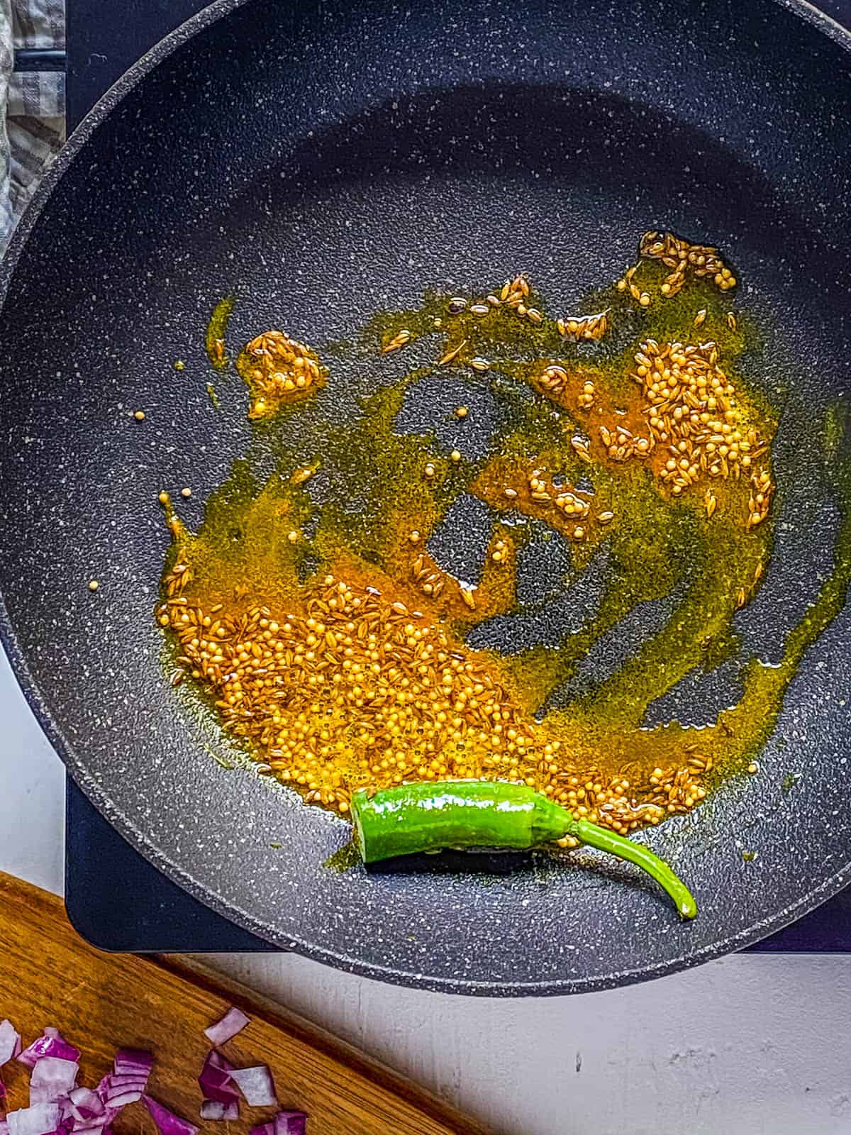 Chiles and Indian spices sauteeing in a pan on the stove.