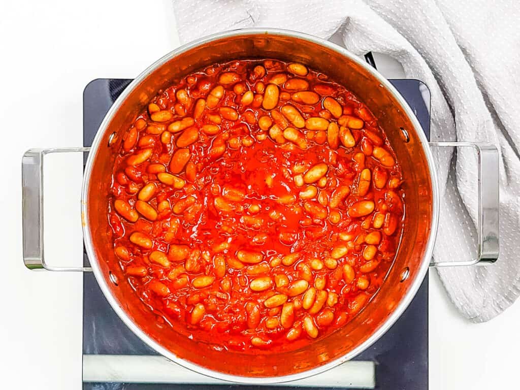 Veget، baked beans, stirred in a large ، on the stove.