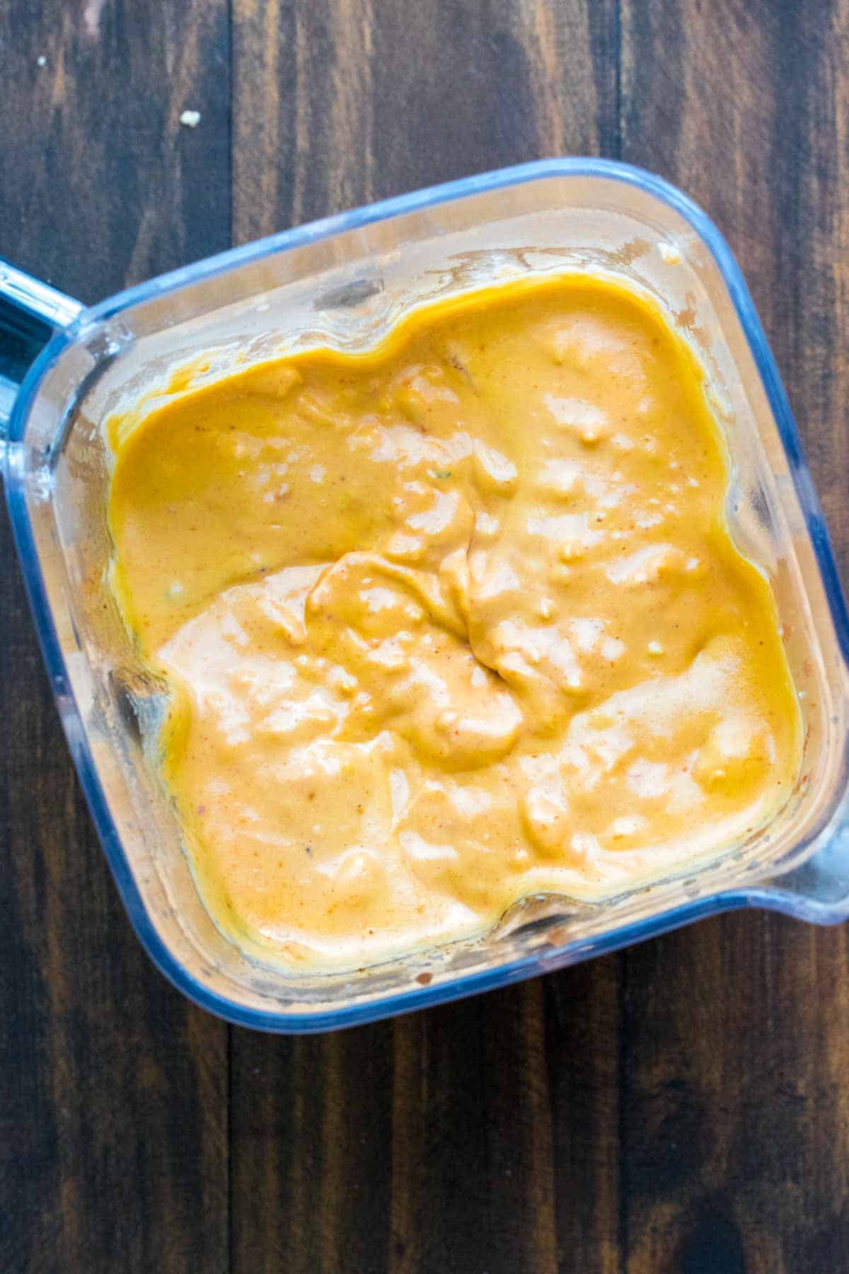 Top view of blender with chunky cauliflower in a creamy orange dip.