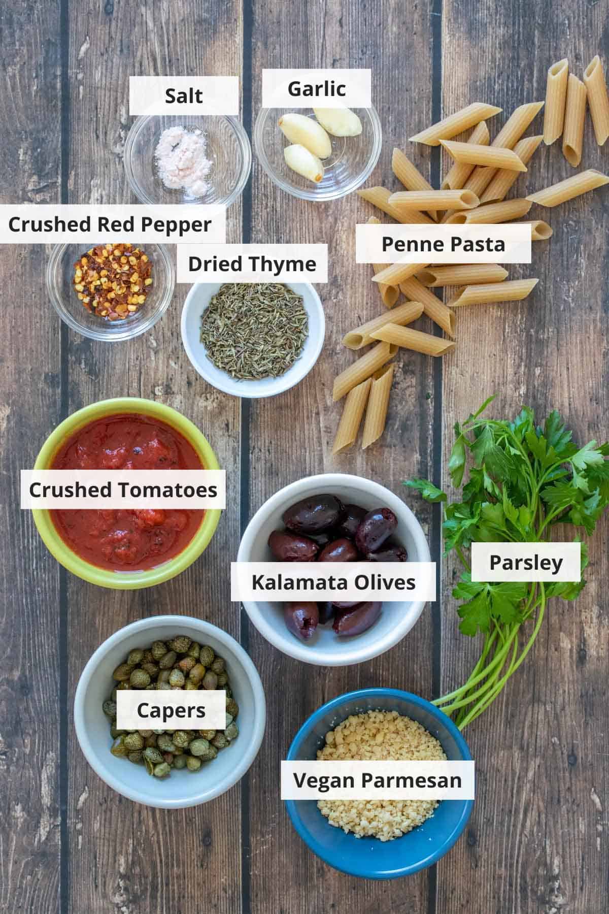 Ingredients for vegan pasta puttanesca recipe on a wood background.
