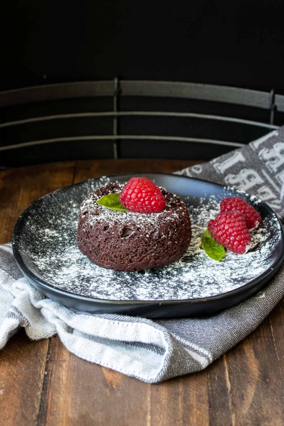 A mini chocolate cake dusted with powdered sugar on a black plate.