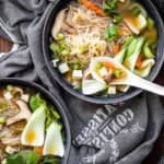 Vegan miso soup served in grey bowls with white spoons on a grey tablecloth.