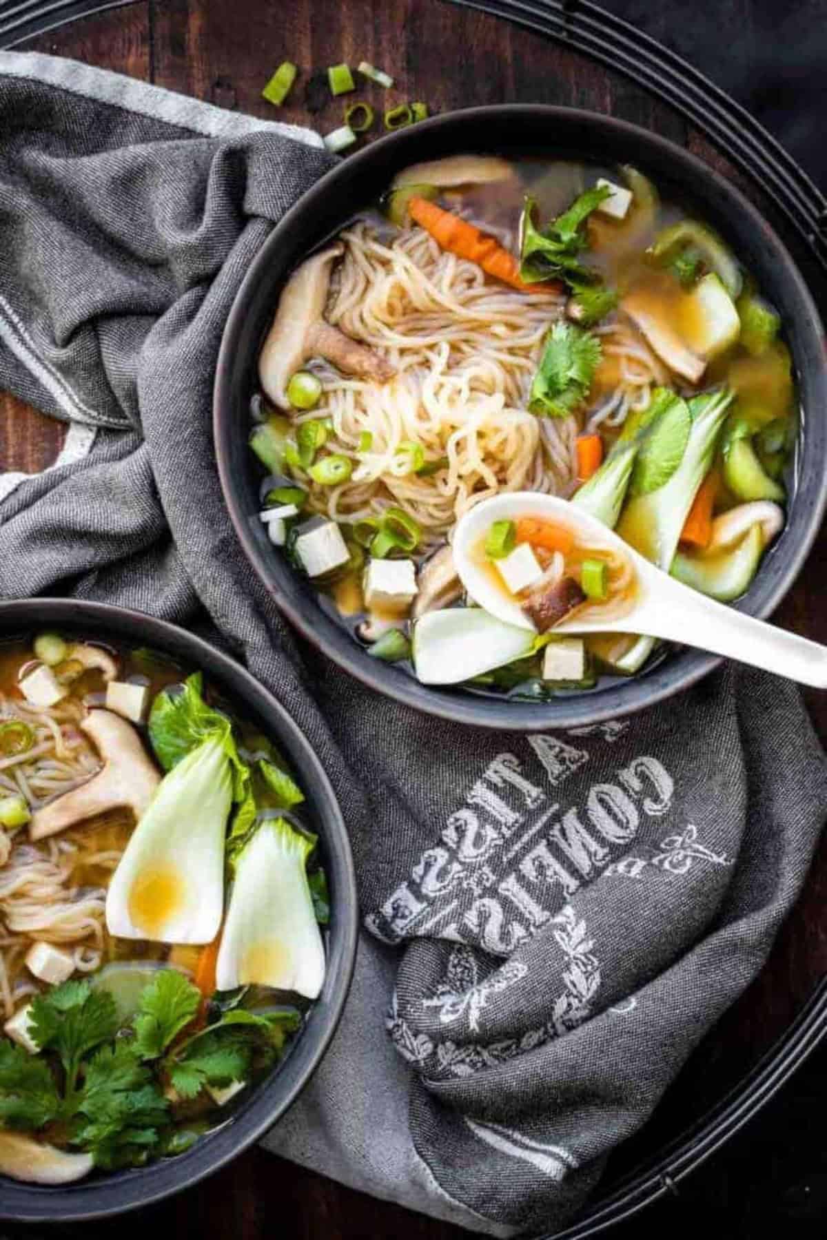 Vegan miso soup served in grey bowls with white spoons on a grey tablecloth.