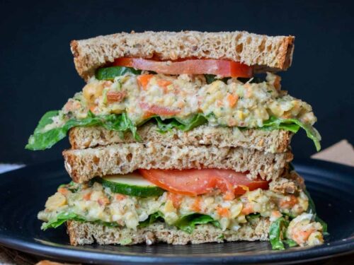 Smashed chickpea salad sandwich filled with lettuce and tomato on whole grain bread