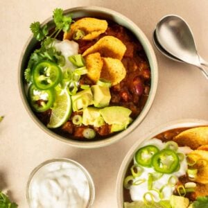 Vegan pumpkin chili in a white bowl with avocado, green onions, tortilla chips, lime, and vegan sour cream as toppings.