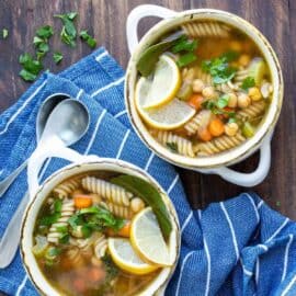 Two bowls of vegan chicken noodle soup side by side, over a blue cloth napkin.