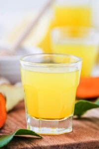 Homemade lemon ginger turmeric wellness shots served in a shot glass on a wooden cutting board.