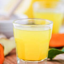 Homemade lemon ginger turmeric wellness shots served in a shot glass on a wooden cutting board.