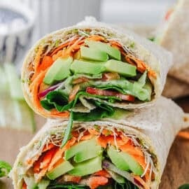 Vegan hummus avocado wrap, cut in half, stacked on a wooden cutting board.