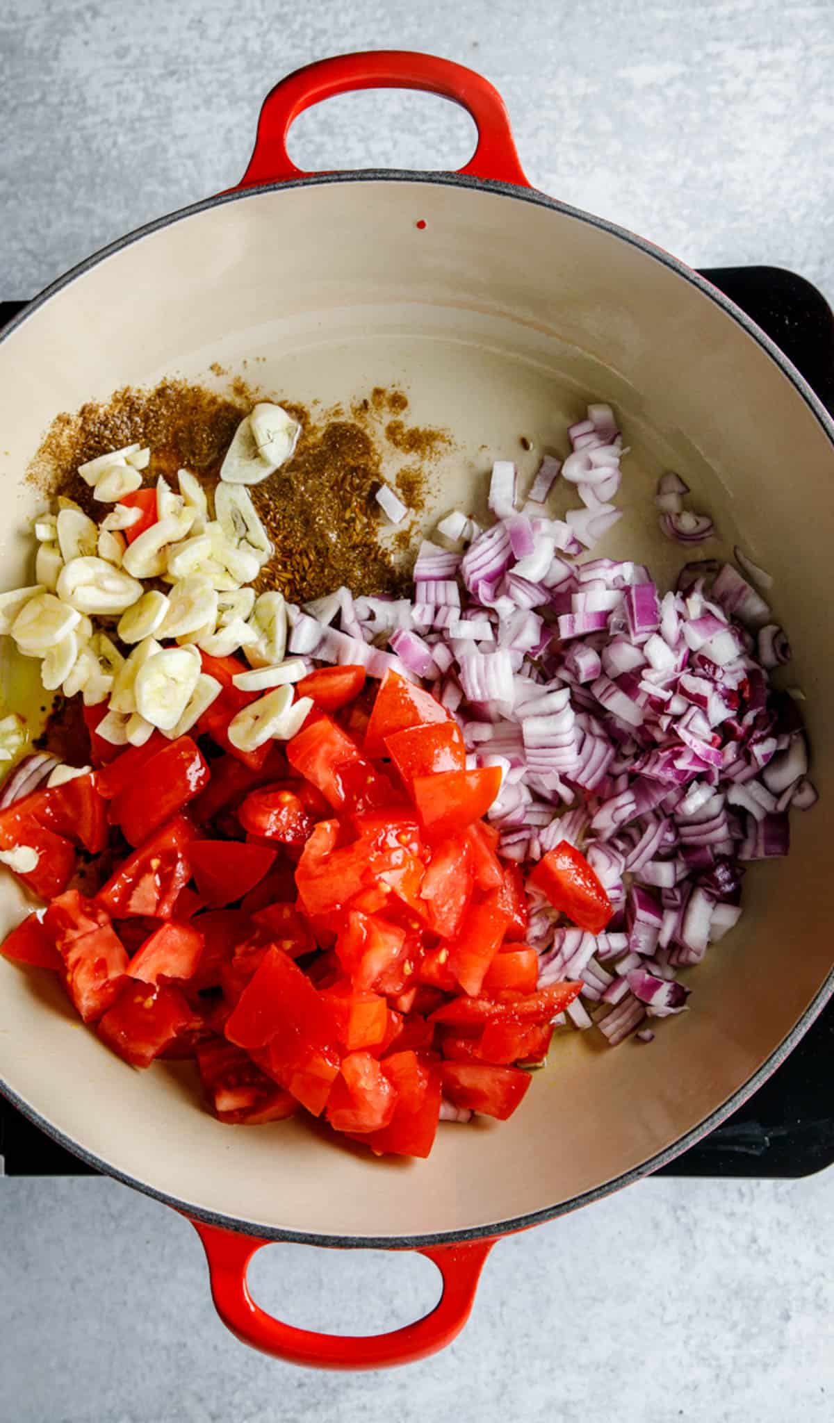 Onions, garlic, tomatoes and spices sauteeing in a pot on the stove.