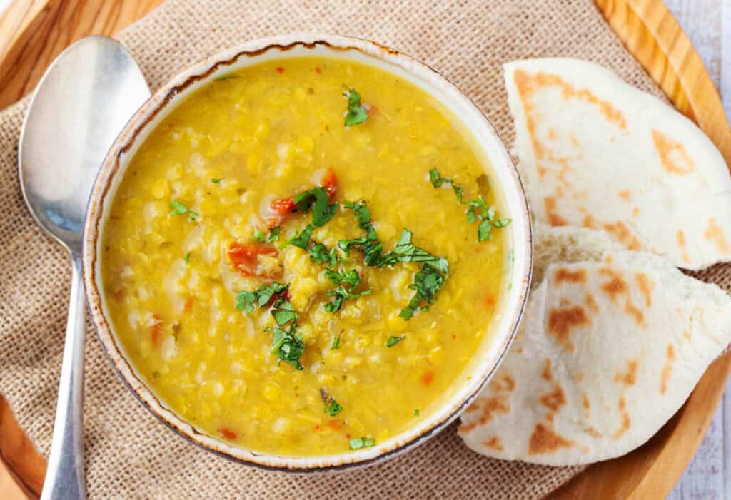 Crock pot dal served in a white bowl, garnished with cilantro, with naan on the side.