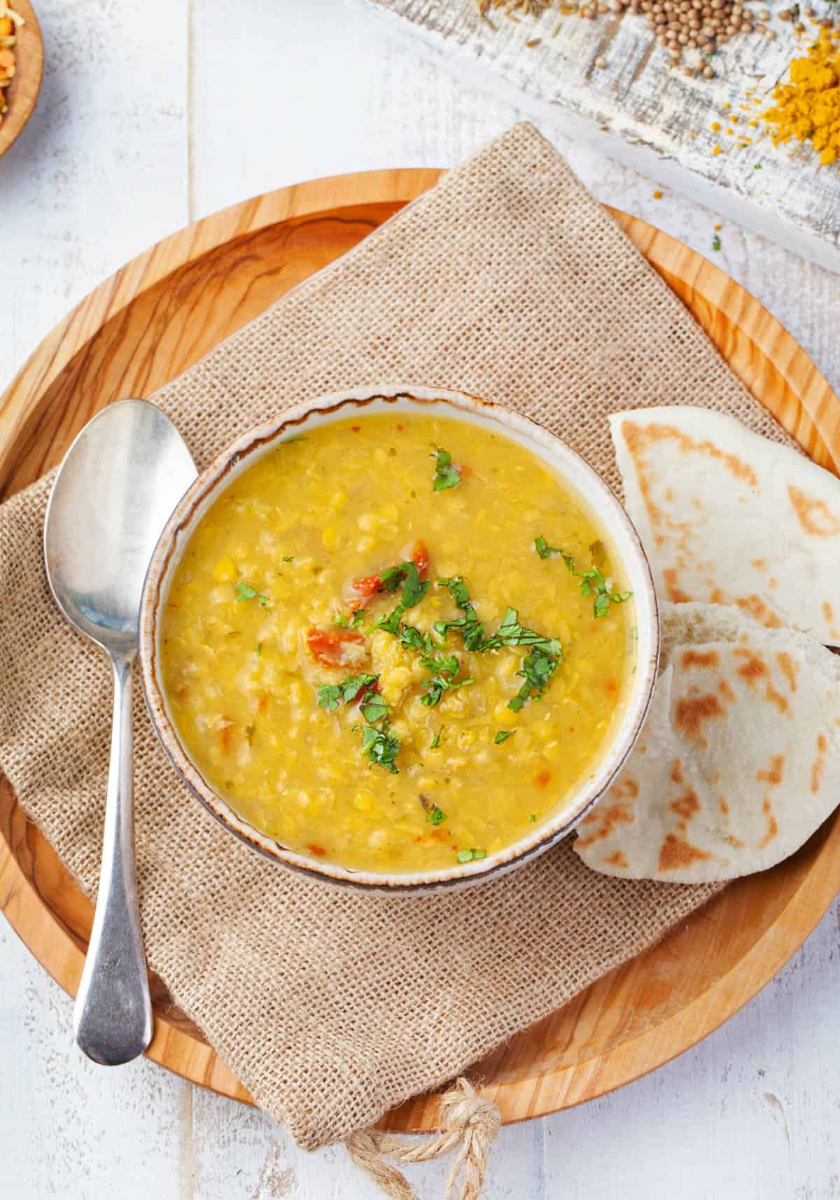 Crock pot yellow dal served in a white bowl, garnished with cilantro, with naan on the side.