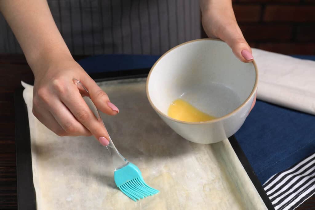 Woman buttering phyllo dough on a table.