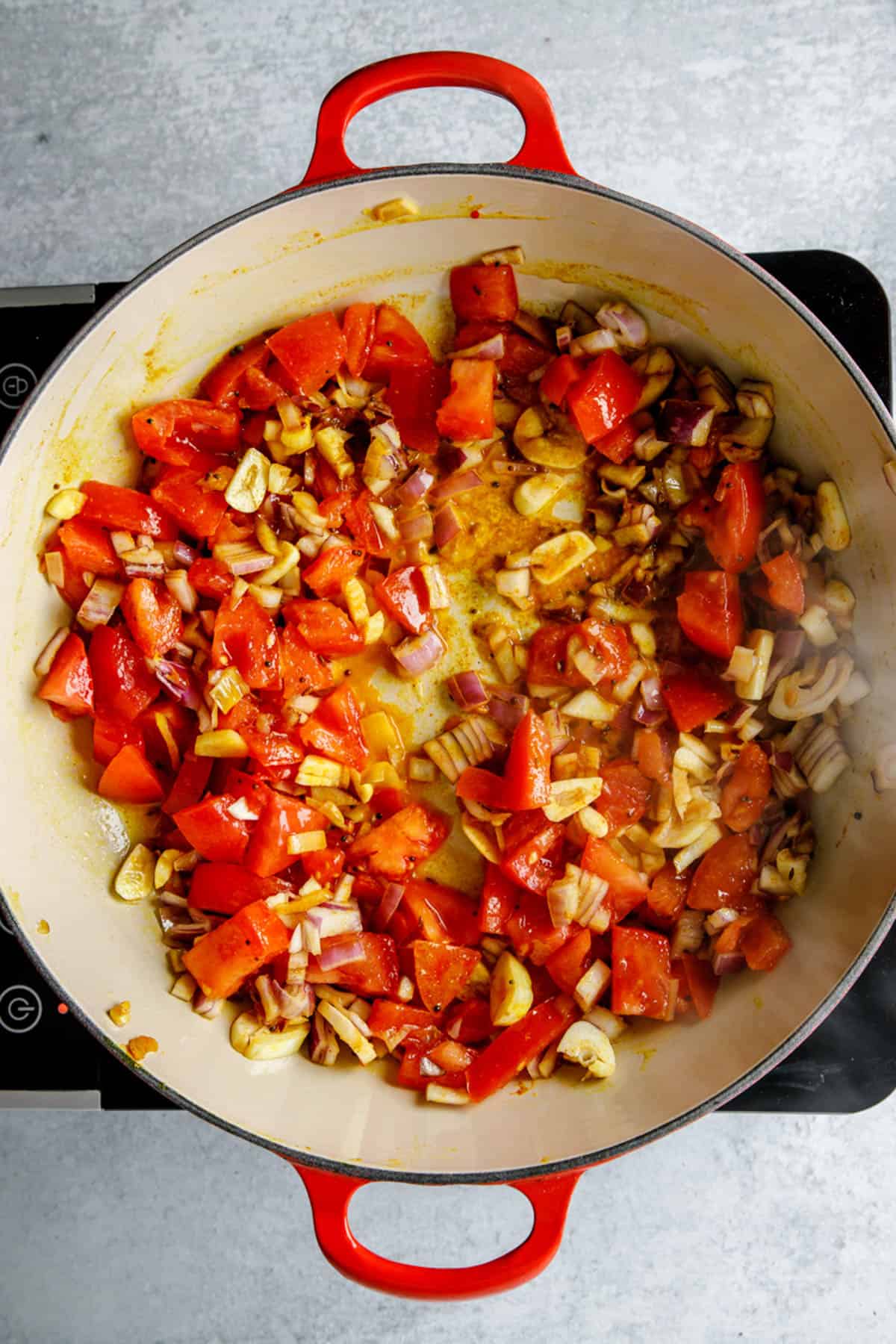 Onions, garlic, tomatoes and spices sauteeing in a pot on the stove.