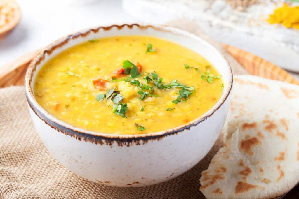 Slow cooker yellow dal served in a white bowl, garnished with cilantro, with naan on the side.