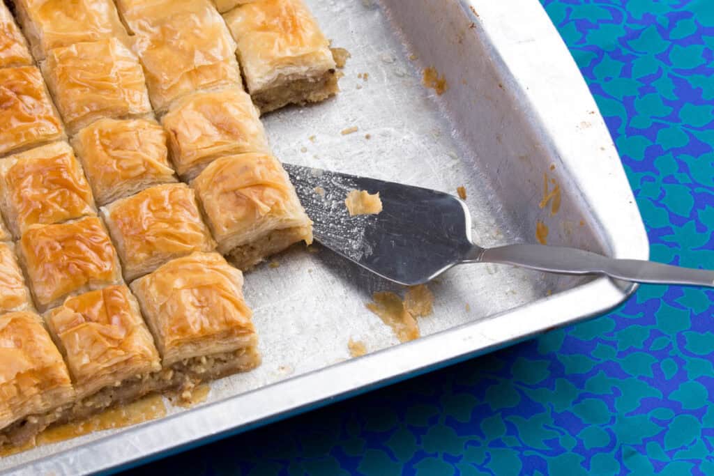 Vegan baklava fresh out of the oven, being served with a serving spoon off a baking sheet.