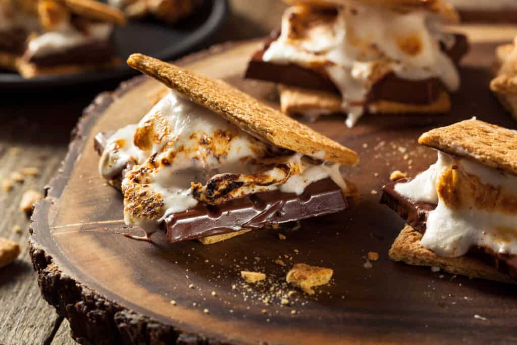 Homemade gooey vegan marshmallow s'mores with chocolate on a wooden cutting board.