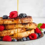 Healthy french toast with berries and syrup served on a white plate.