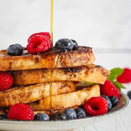 Healthy french toast with berries and syrup served on a white plate.