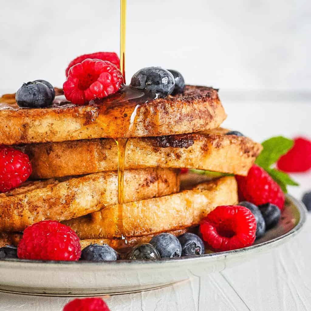 Low sugar french toast with berries and syrup served on a white plate.