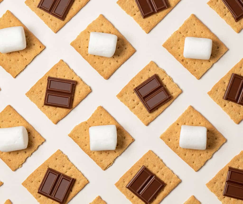 Graham cracker squares with chocolate pieces, vegan marshmallows on a white background.