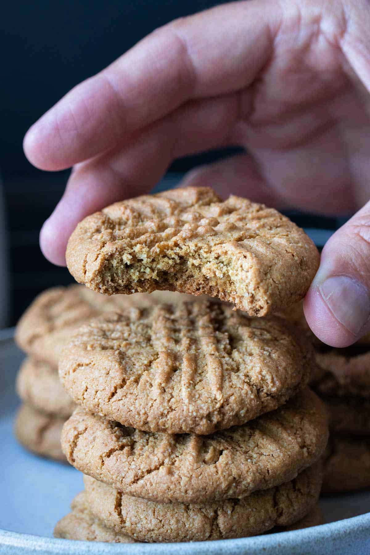 Hand holding a vegan gf peanut butter cookie over a stack of cookies.